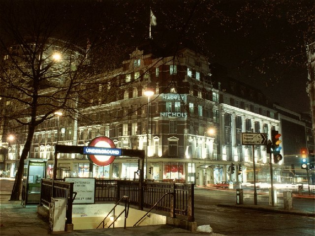 night-time scene of steps down to station with street of grand, illuminated shops in background