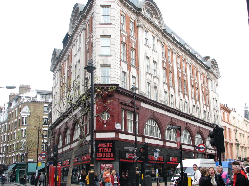 maroon-painted station-entrance, formed as two series of arches meeting at an acute angle at a street corner