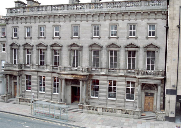 wide, grand flat-fronted pale grey building with three doors, each flanked by pillars and with steps up