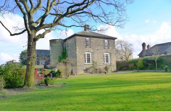 view across green lawn towards squarish grey Regency house with a tower on its left side, and a large tree at left of frame