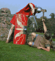 animation showing John at 62 wearing a sackcloth tunic over a light blue shirt and shorts, sprawled on his back on grass clutching a hammer-shaped chunk of branch and repeatedly bonking a red-uniformed Roman soldier on the helmet with it, as the soldier bends down over him and tries to stab him with a sword