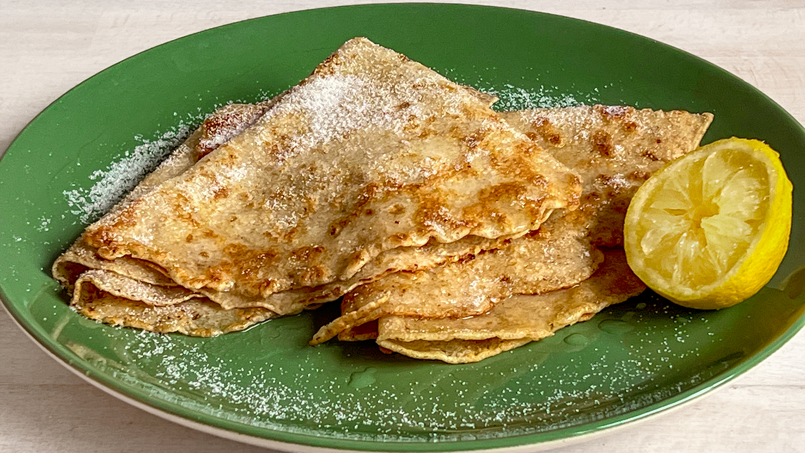 photo of two pancakes folded into triangles on a plate, with half a lemon