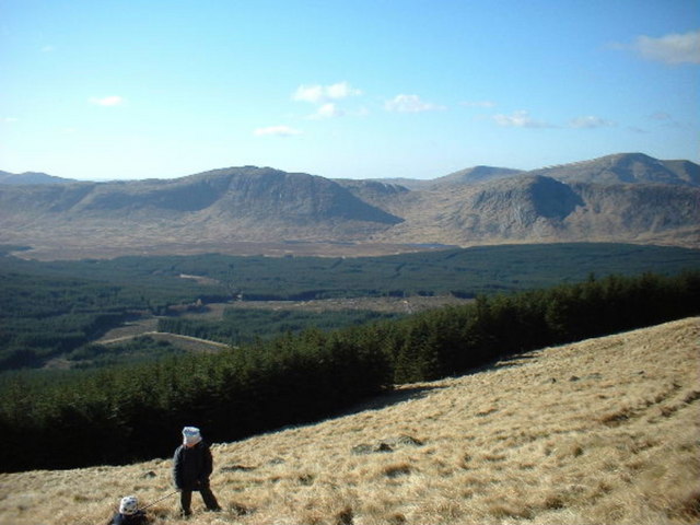 view from a high place across a small, wooded plain towards a high bare ring of hills in the distance