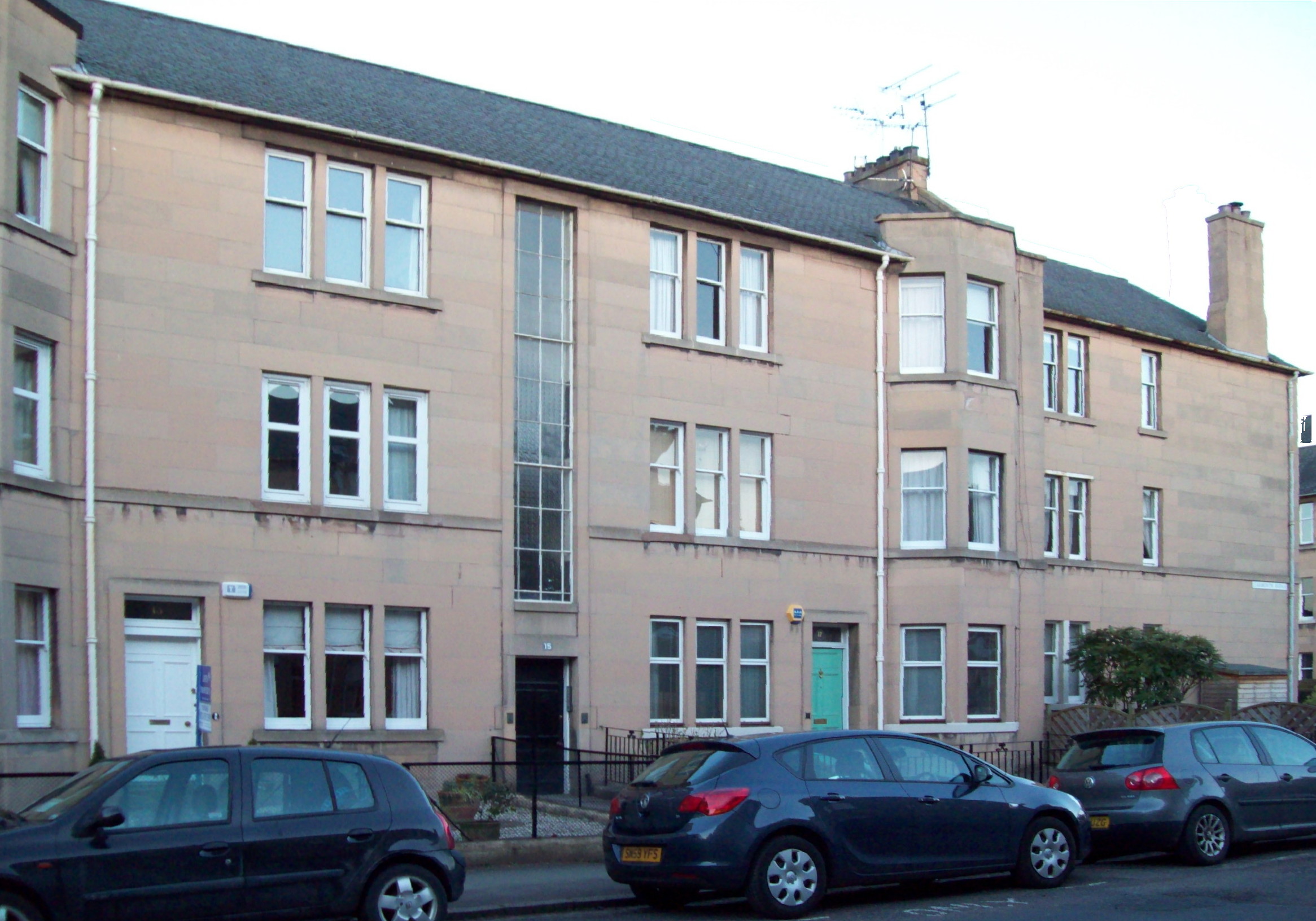 terrace of three-storey, fawn buildings in a blocky Art Deco style, with flat fronts broken up by columns of bay windows and 2½-storey-high narrow oblong windows