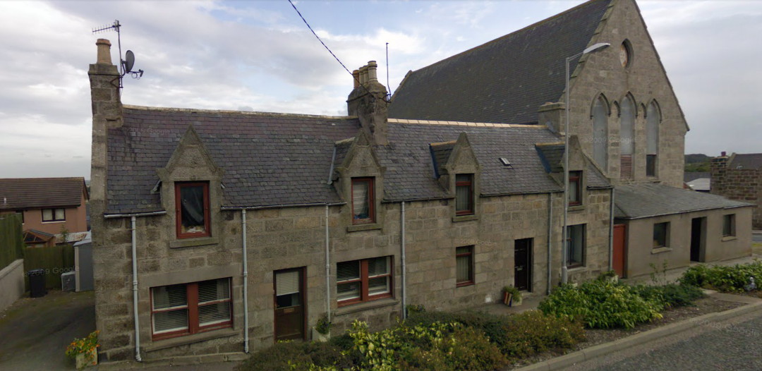 photograph showing a small, plain church on a corner, terraced with two stone Victorian two-storey houses with dormer windows on the first floor