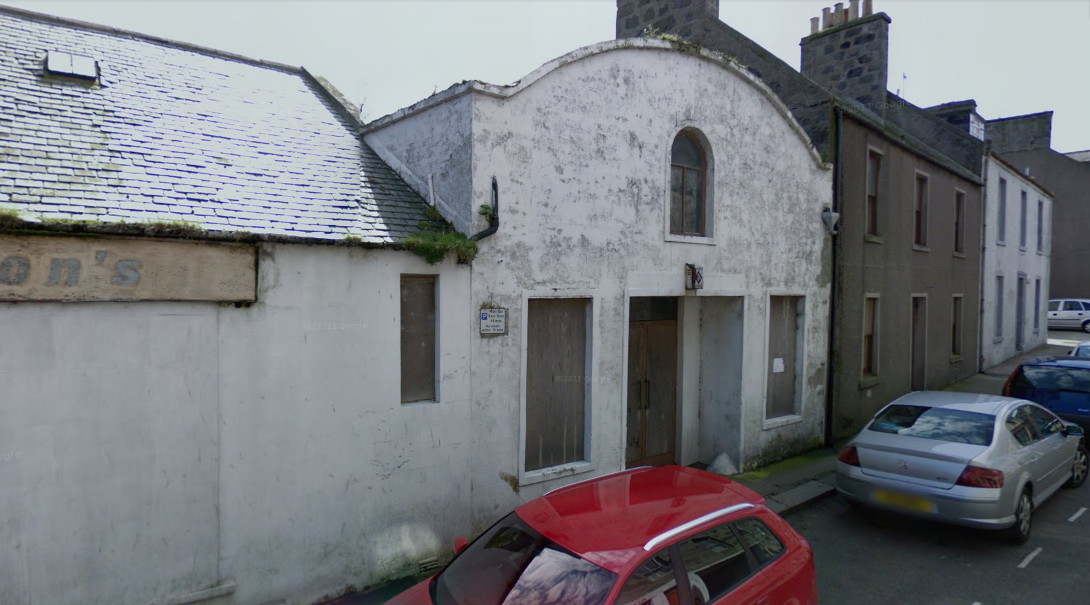 View along and across a narrow street to a long white building with an arched roof over the farthest section