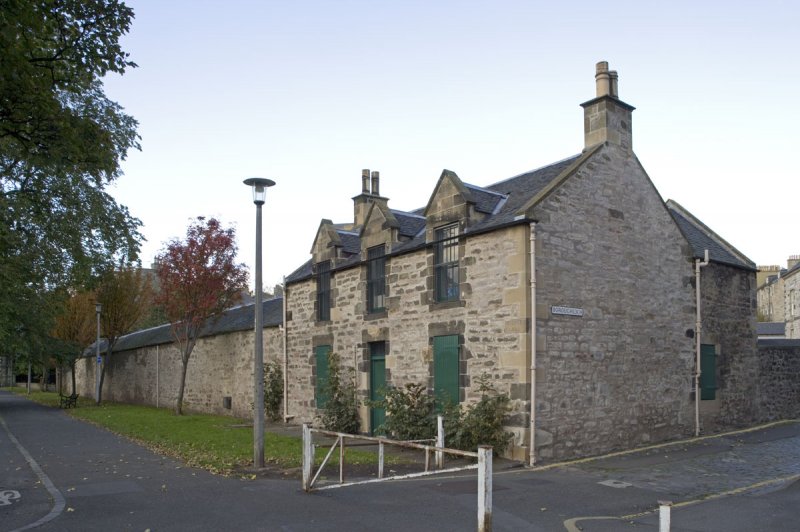 photo\' showing a small, squarish 18th C stone building with its windows boarded up, seen corner-on, with a very long low windowless barn-like building extending behind it