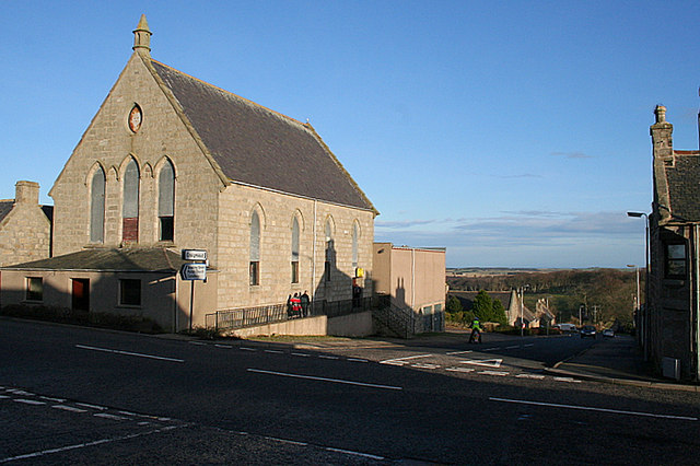 view down a steep road towards woods and farmland, with the sea in the far distance and a church on the corner of the road in the left foreground