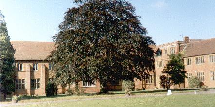 long low Victorian and later buildings in ginger brick, surrounding a grassy area with trees