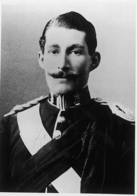 greyscale head-and-shoulders photograph of a handsome young man in dress uniform, with slicked-back hair and a long, pleasant, serious face partially obscured by a handlebar moustache