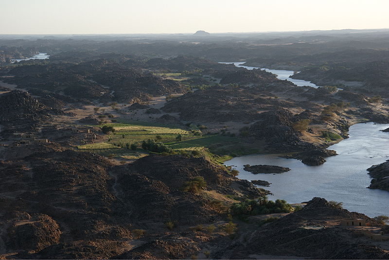 view from a high place looking down at a river winding across a landscape of small fields tucked in amongst outcrops of rough black rock