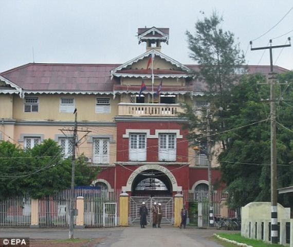 large three-storey, brightly-coloured building resembling a Victorian hotel, with a tunnel through the centre of the building, and a wire fence and guards in front