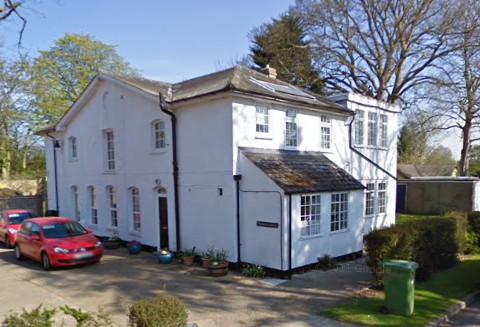 corner view of a white two-storey building with a front-facing peaked roof flanked by sections at right-angles, and with the windows arranged rather like a face