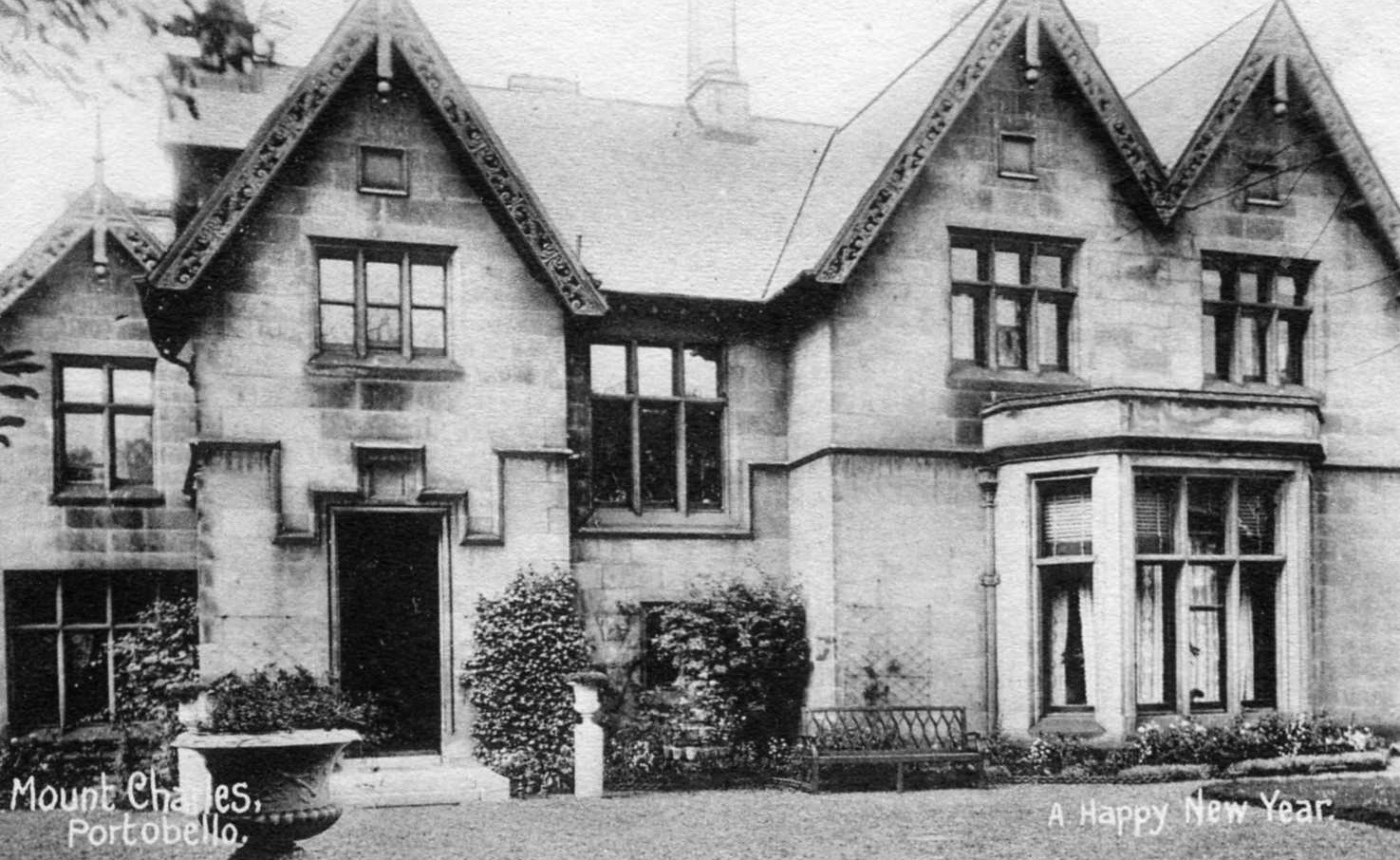 greyscale photographic postcard of a very large rambling Victorian house with four gabled roofs visible, and a large bay window looking onto a formal garden