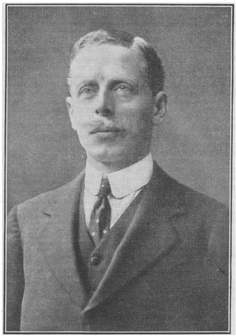 greyscale newspaper photo\' of a dapper, suited man with a high collar and a fair moustache