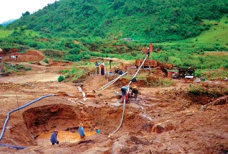 view across an area of tan ground pocked with craters, towards a slope covered with green jungle