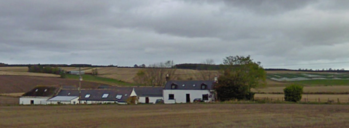 view across fields to a cluster of low white buildings under a lowering sky