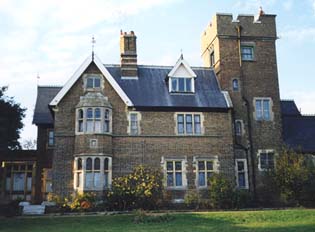 view of a Victorian Gothic building in beige brick with a peaked gable on the left and a square tower on the right