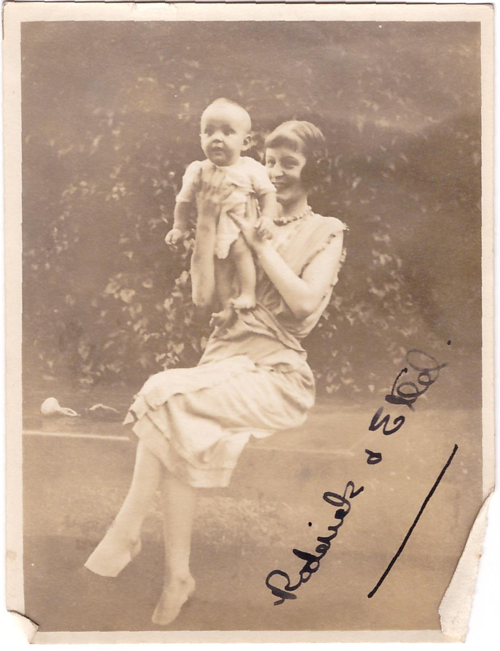 Ethel sits on a garden step or wall, holding up baby Rory
