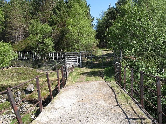 view of small bridge over stream, leading to a path which has trees either side but only for a short way