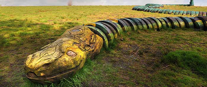 photo\' of giant sculpture of a snake, with a head of gilded driftwood and a body made of painted tyres, stretched across an expanse of grass