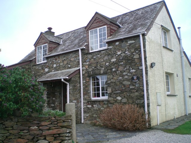 two-storey cottage with dormer windows and enclosed porch, having a white end-wall and the front face left as bare, crazy-paved grey stone