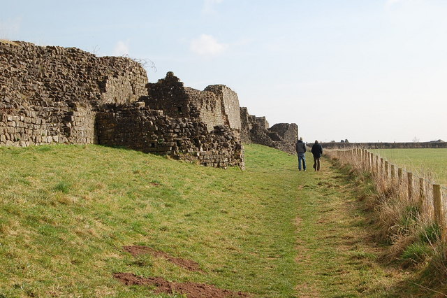 the massive but broken and jagged remains of a long stone wall with towers, with a grassy slope tending down to the right