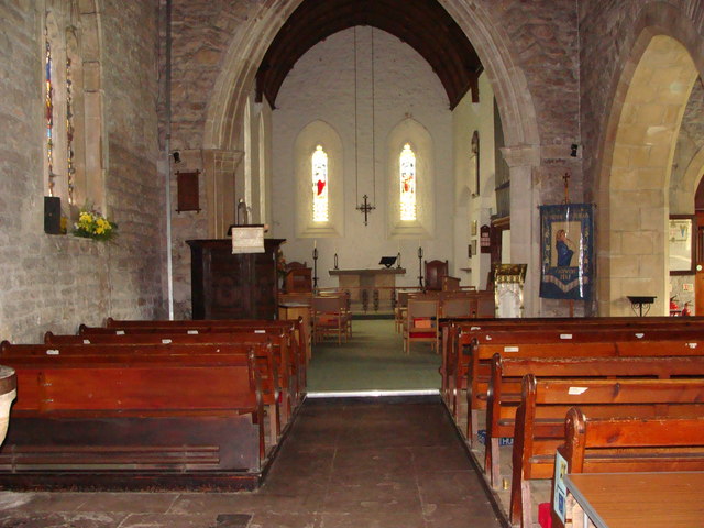 interior of small, ancient church, looking down an aisle between rows of pews towards a stone arch through which can be seen a small altar, with another arch on the right
