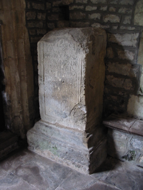 broken stump of stone on a tiered plinth, covered with Roman lettering, tucked into the angle inside a church door