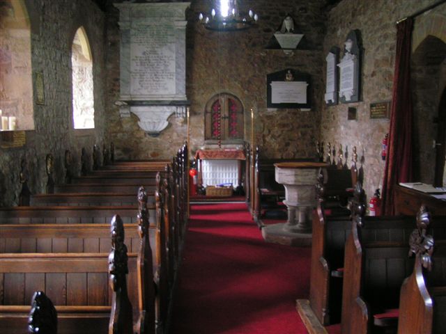 interior of small, ancient church, looking down an aisle between rows of ancient pews towards a small altar, with deep window embrasures on the left and a stone font on the right