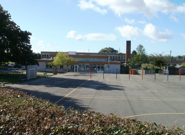 view across a concrete playground to a long low blocky building in tan with strips of white windows and a free-standing chimney at the right