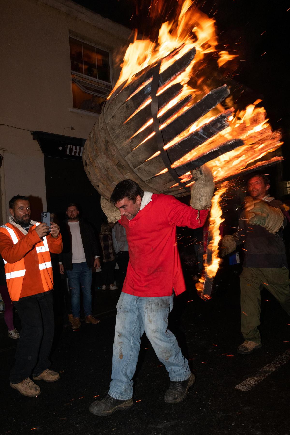 Photo of man carrying a burning, disintegrating barrel on his back