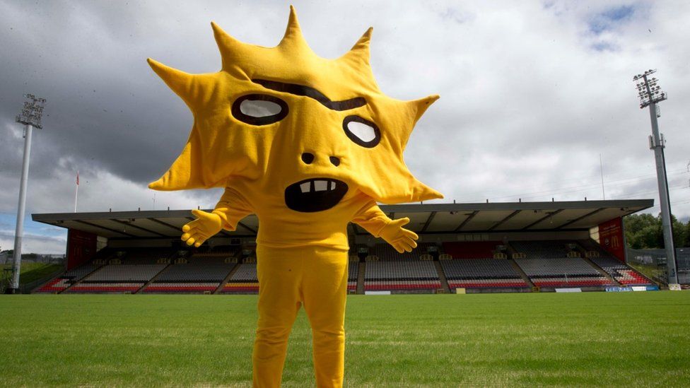 Photo of somebody dressed all in yellow, their head and upper body encased in a kind of spiky cloth sunburst with a gaping, toothy mouth and blank, staring eyes