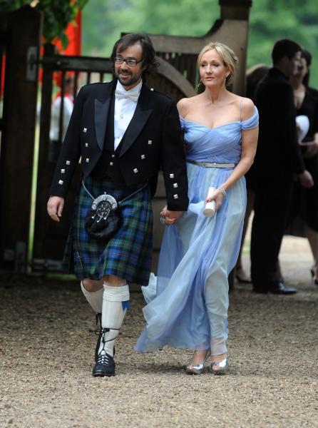 photo showing a swarthy many in spectacles, wearing full Highland dress including a blue and green kilt, holding hands with a tall blonde woman wearing a floaty, off-the-shoulder pale blue dress