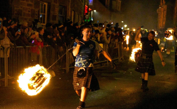 Photo of men in kilts swinging balls of fire on long chains