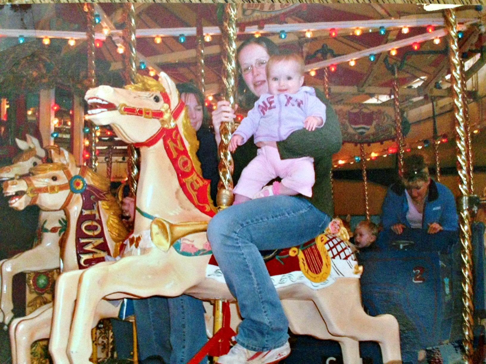Photo of a mother and child riding a white and red merry-go-round horse