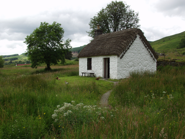 tiny, white-painted one-room thatched cottage with a small lawn in front, set on a slope covered with long grass, heather and trees
