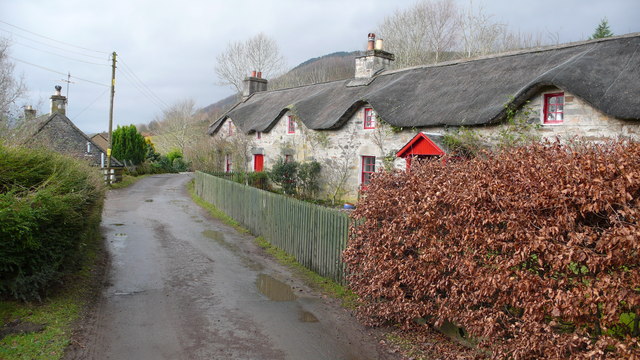 lane leading into the distance, with an ordinary stone house seen end-on on the left, and on the right a terraced row of rough-walled two-storey cottages with dark thatch coming down low and looking like eyebrows