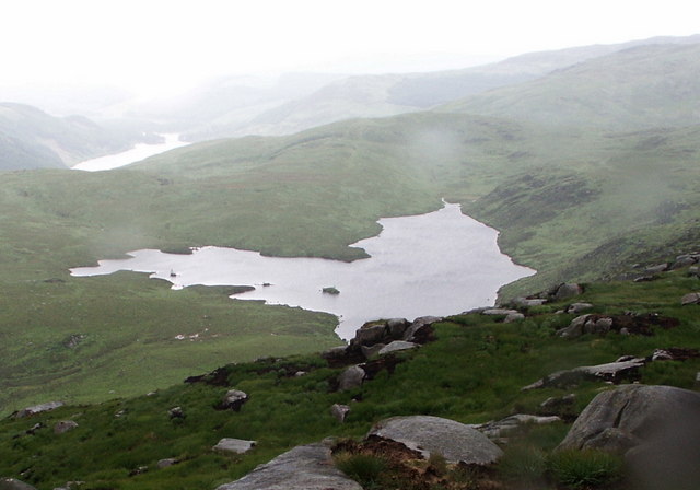 small irregular lake reflecting the sky, set high up among rolling green hills blurred by mist