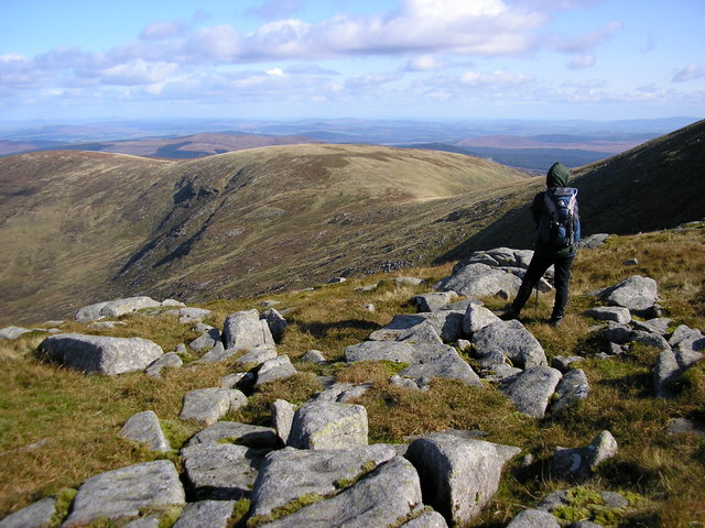 view across stony ground towards rolling grey-brown hills, with a hiker in the foreground