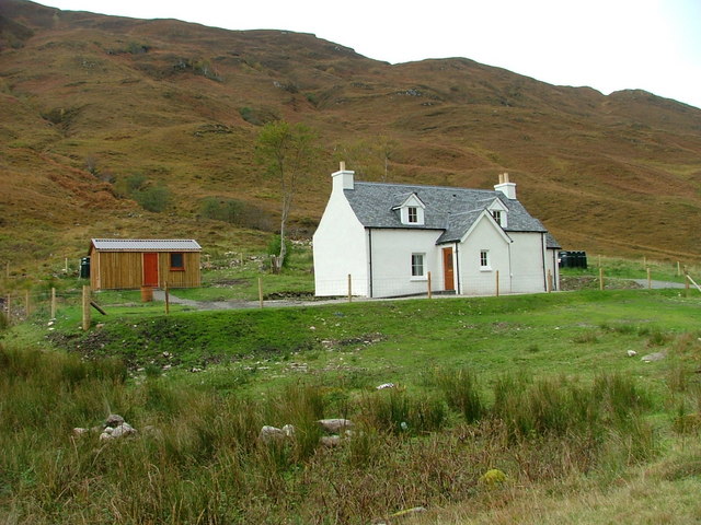 small white-pinted two-storey building with dormer windows, with golden-brown, bracken-covered slope rising behind it