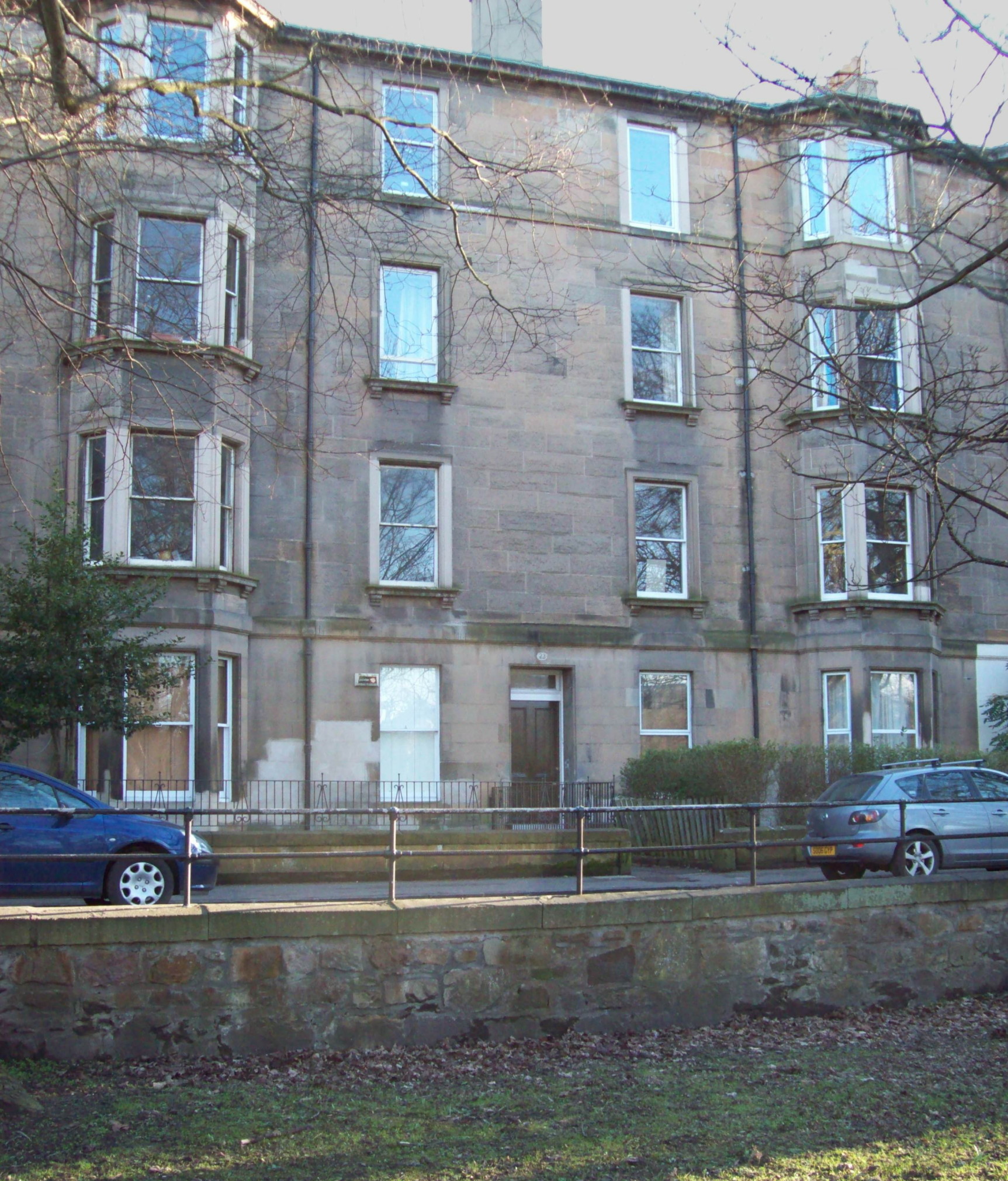 view of a terrace of four-storey beige stone buildings, with flat fronts alternating with double columns of bay windows, and a door into the flat part