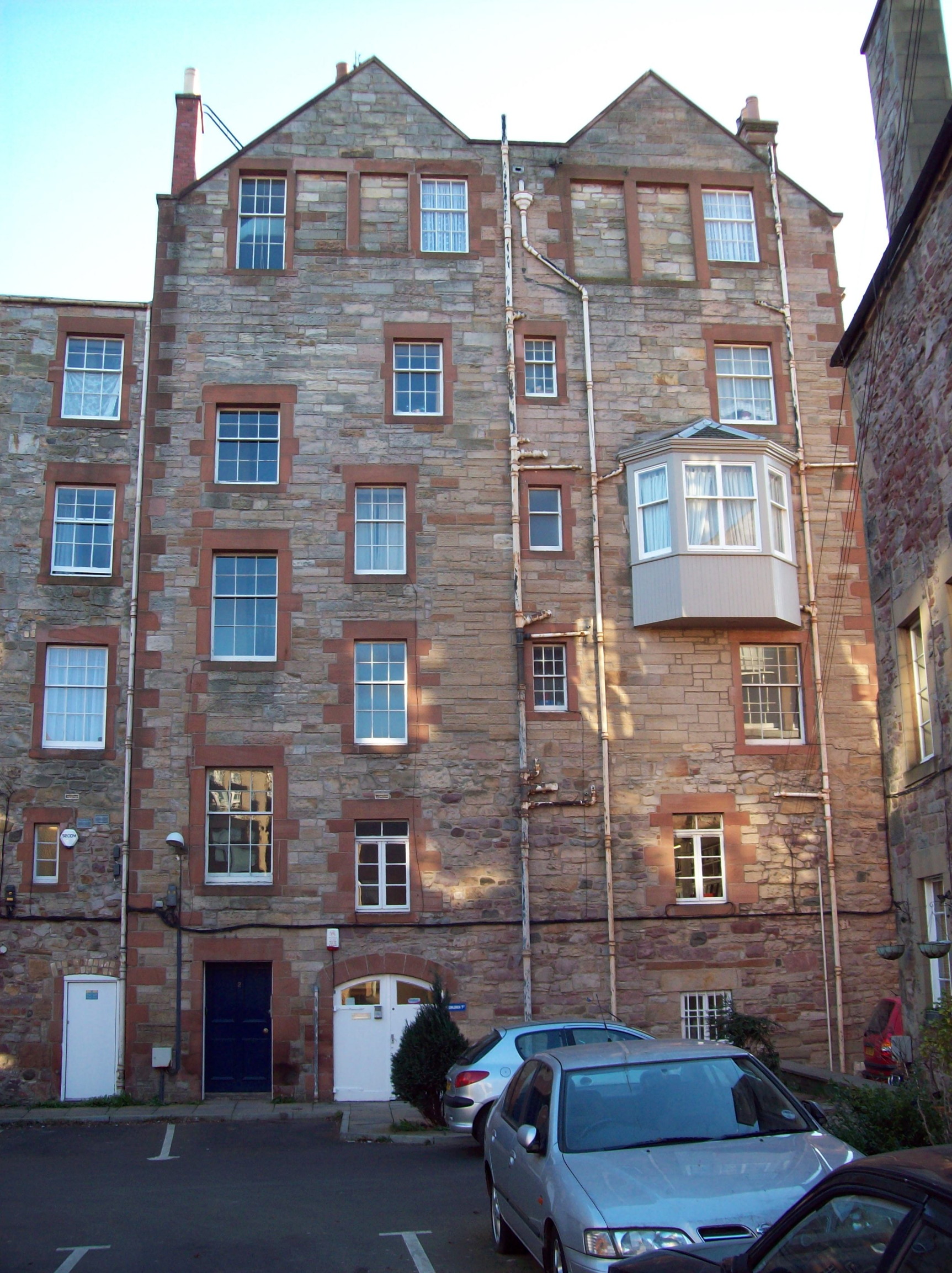 five-storey building in ginger stone with red sandstone trim around the windows and a double triangular roof