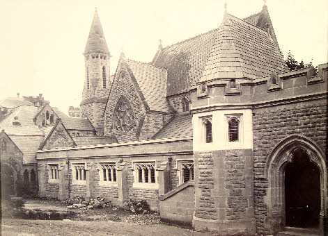 black and white photo\' of Victorian Gothic church made of small stones, with elaborate Mediaeval-style towers, windows, arched doors and crenellated roofs