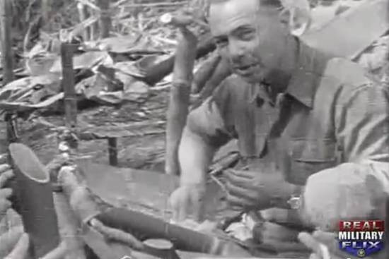 greyscale photo\' showing a strongly-built man in an army shirt, with dark receding hair, with eatibg rice with his hands from a bamboo dish