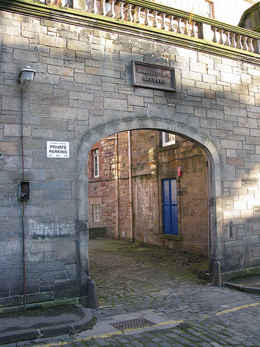 stone archway with balustrade along the top and a carved sign saying \'Boroughloch Brewery\', leading to a cobbled courtyard and buildings of red-brown sandstone