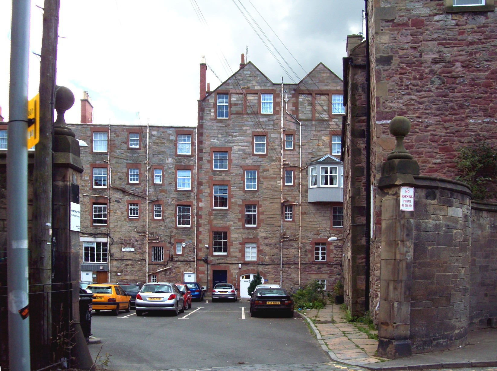 view between stone pillars into a courtyyard lined with multi-storey buildings made of a gingerish stone, with red sandstone rims round the windows