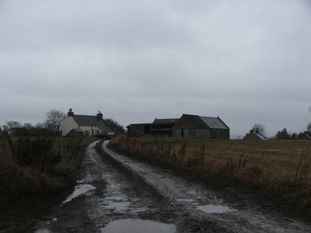photograph looking along a muddy track on a dark evening, towards a white cottage and a cluster of barns