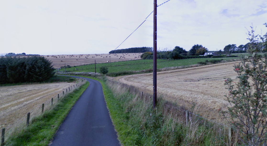 view across fields with a small group of buildings up a slope in the right distance