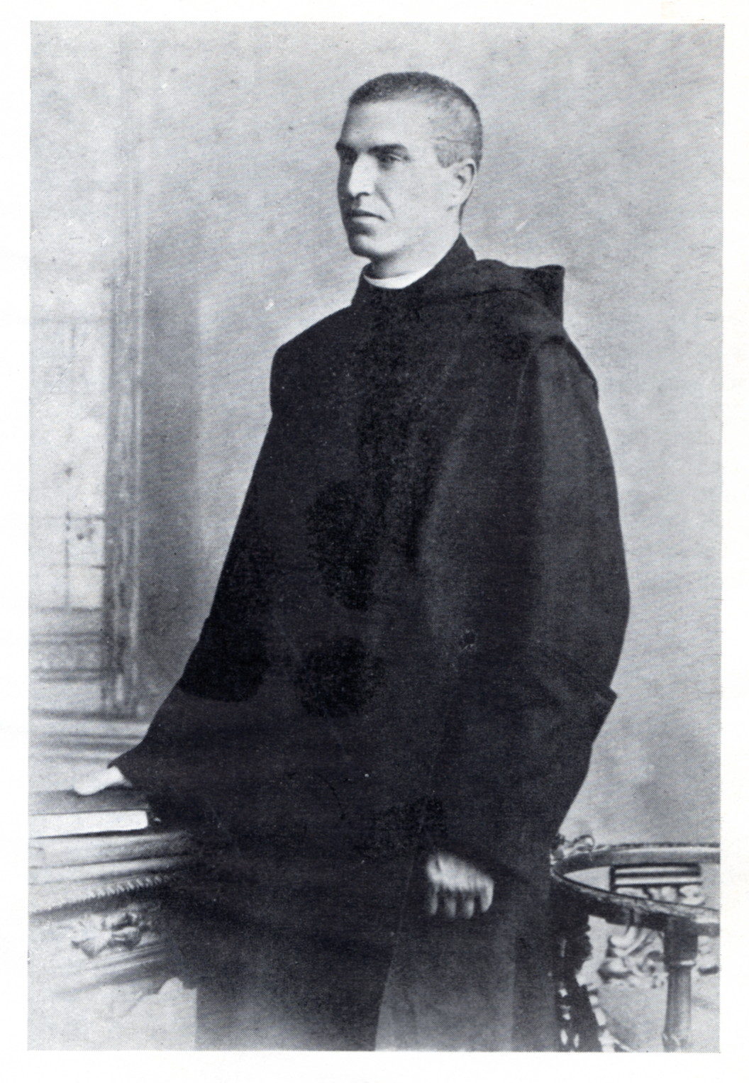greyscale three-quarter-length photo\' of a stern-looking, crop-haired young man wearing dark robes